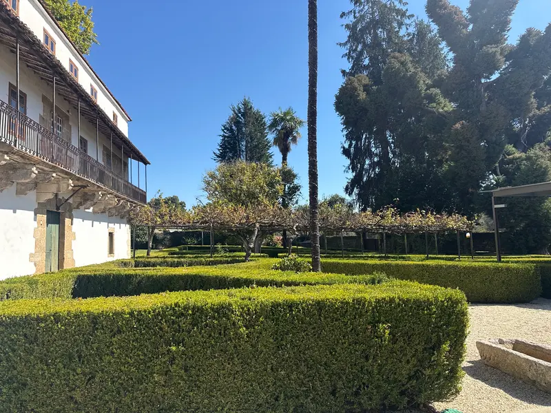 Parterres de boj y una palmera junto a la fachada del pazo con su galería de hierro
