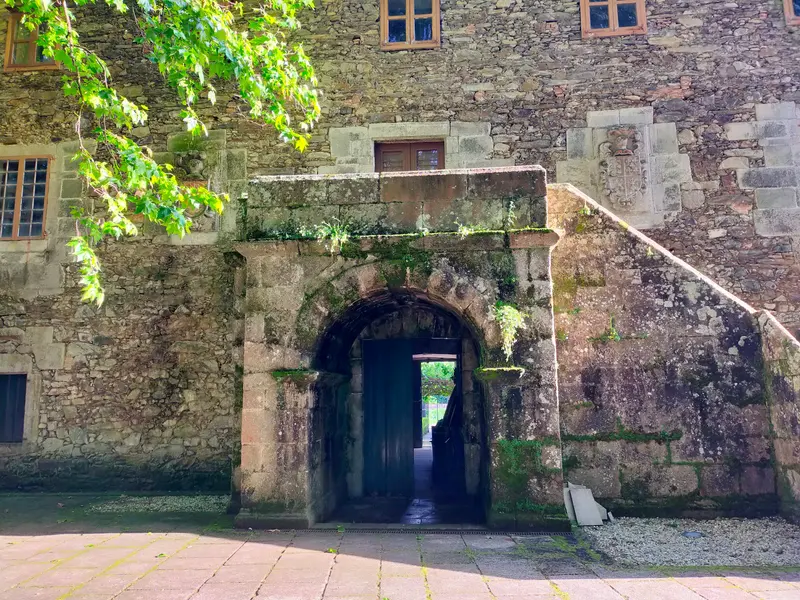Fachada de piedra del pazo con el paso en arco y la escalera exterior de granito