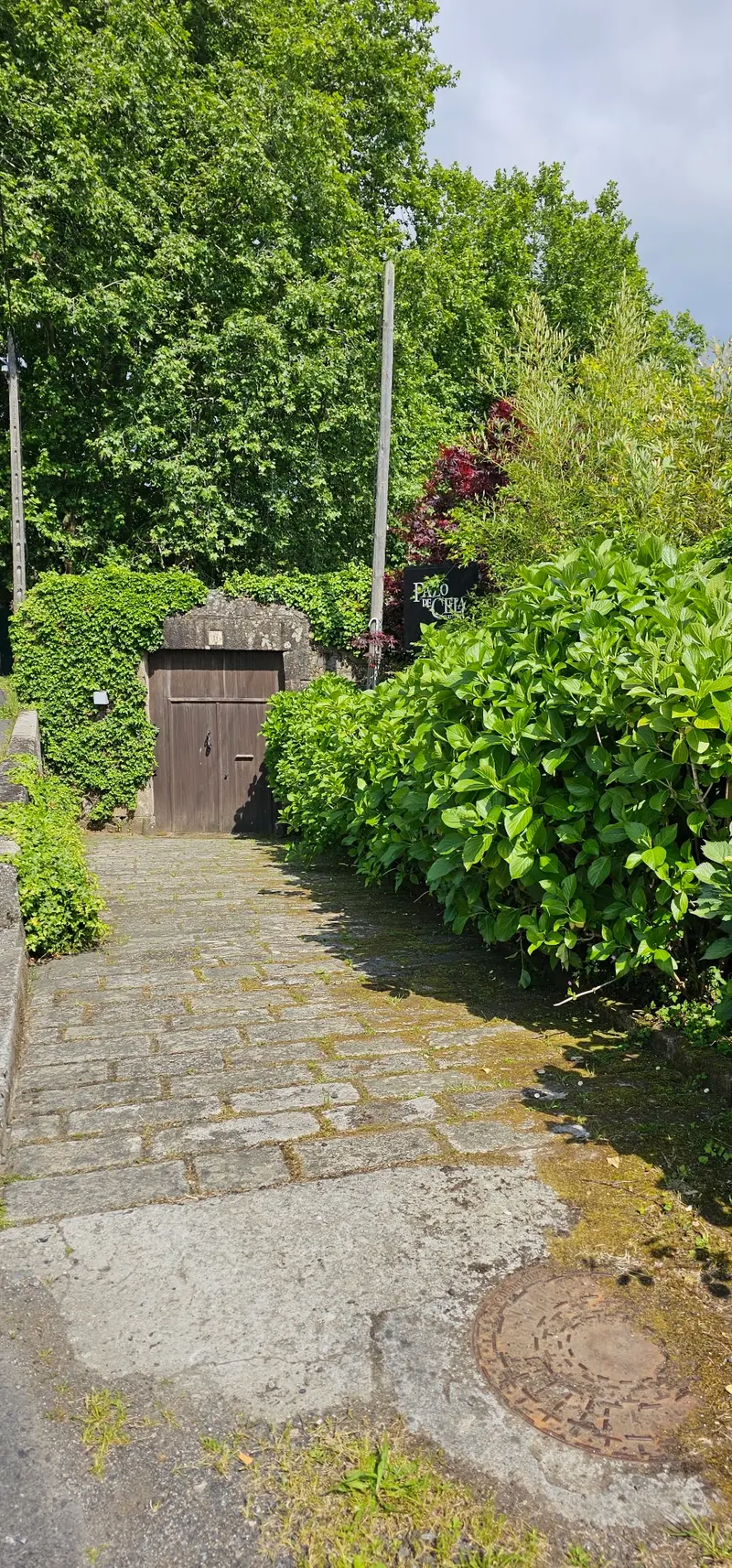 Camino de piedra entre setos hasta una puerta de madera en el muro de la finca