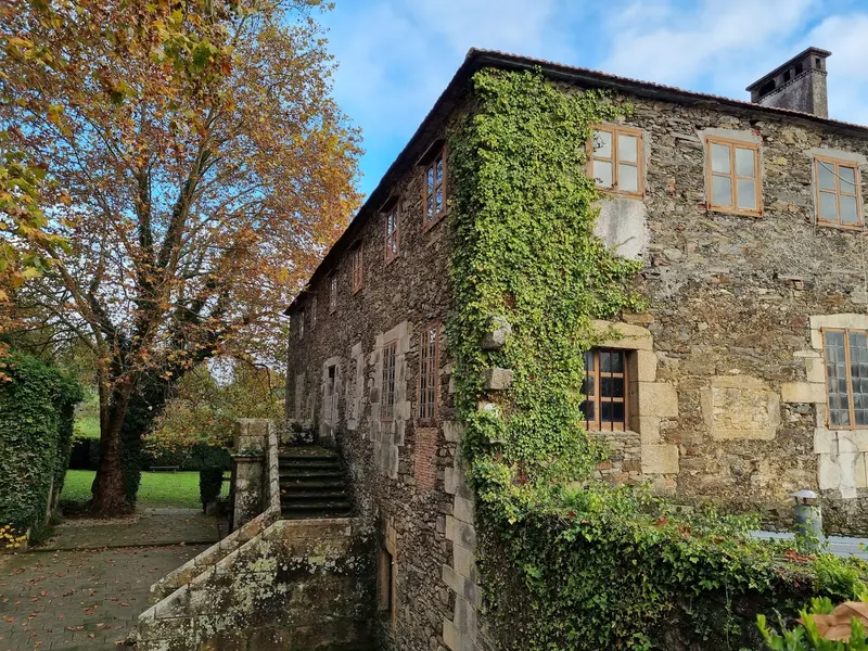 Fachada de piedra del pazo con hiedra y escalera exterior, en otoño